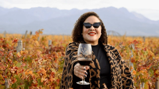 Pati segurando uma taça de vinho em meio a uma paisagem outonal em Mendoza, Argentina